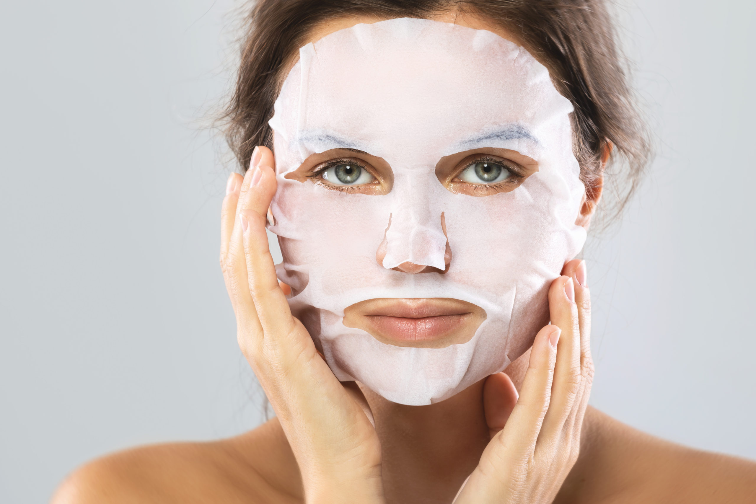 Face care and beauty treatments. Woman with a sheet moisturizing mask on her face isolated on gray background