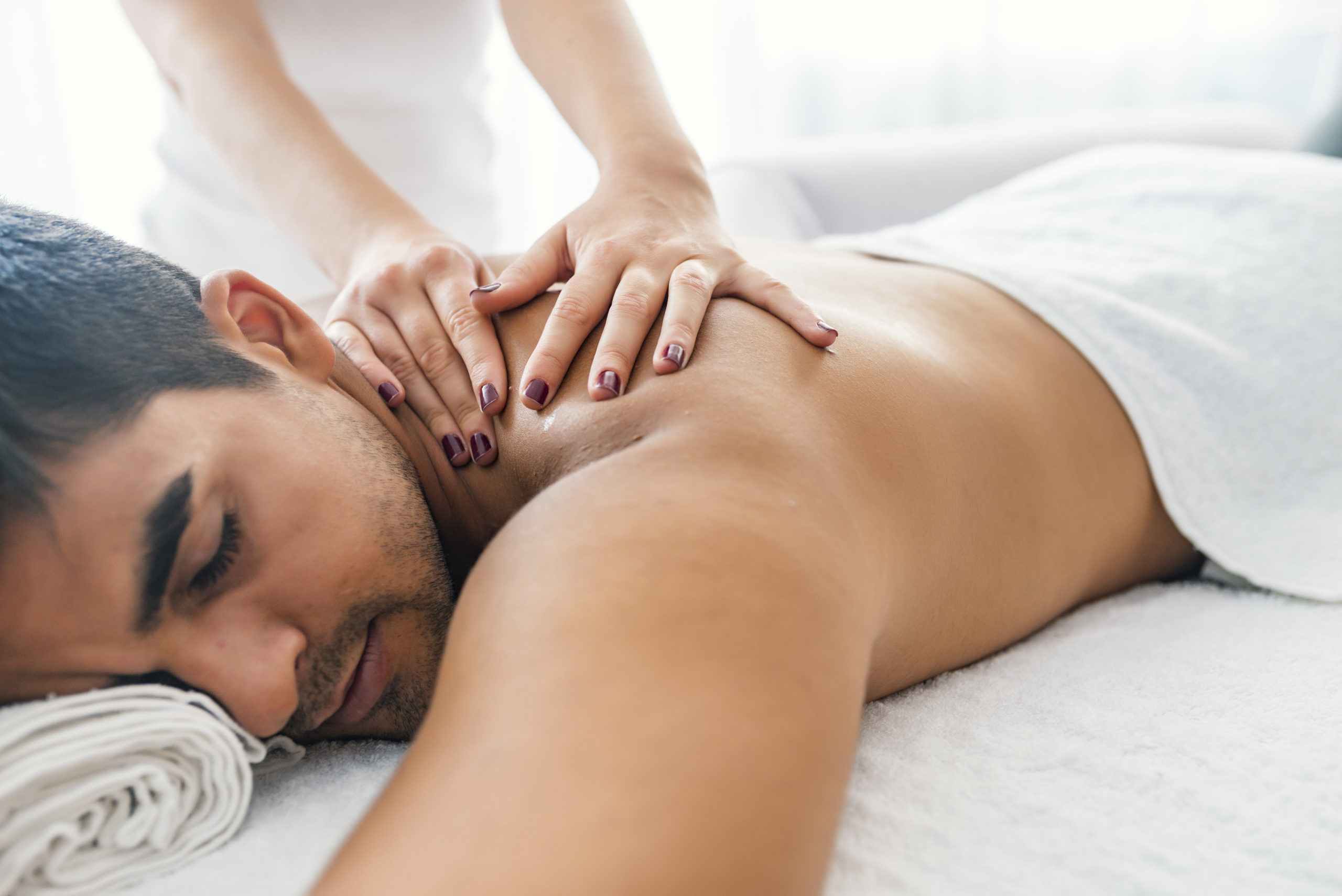 Young man is enjoying massage on spa treatment. Man having a massage in a wellness center. Handsome man receiving back massage in spa salon. Man relaxing in a wellness center